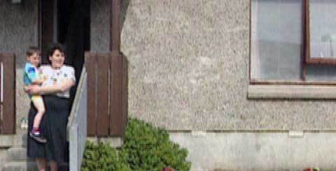 a woman outside a house with a child on her hip